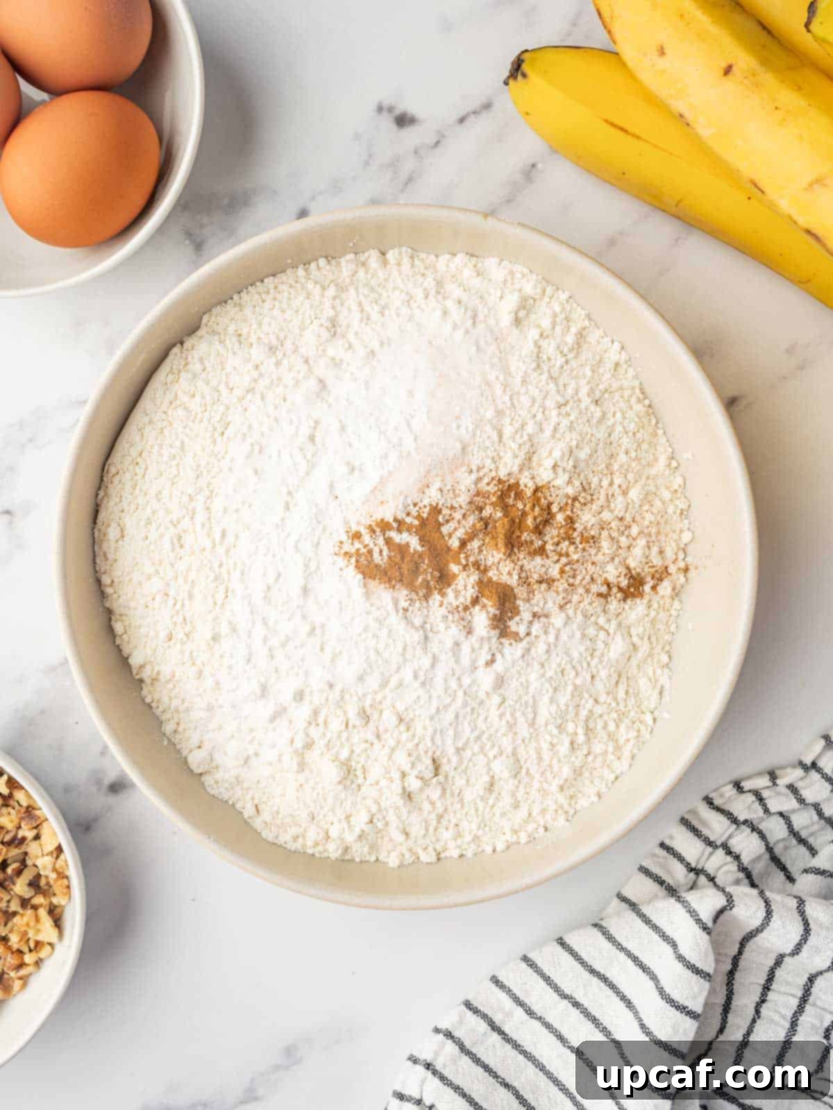 Close-up of a bowl filled with various dry cake ingredients, including flour, cinnamon, and leavening agents.