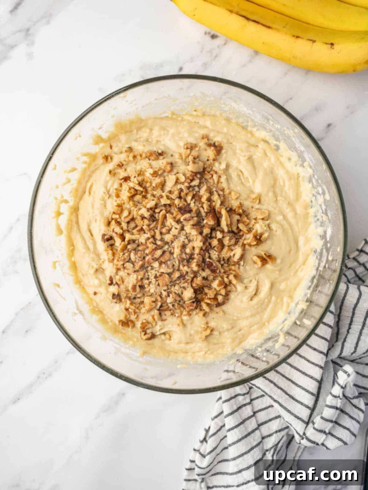 Close-up shot of chopped walnuts being folded into a thick, creamy cake batter.