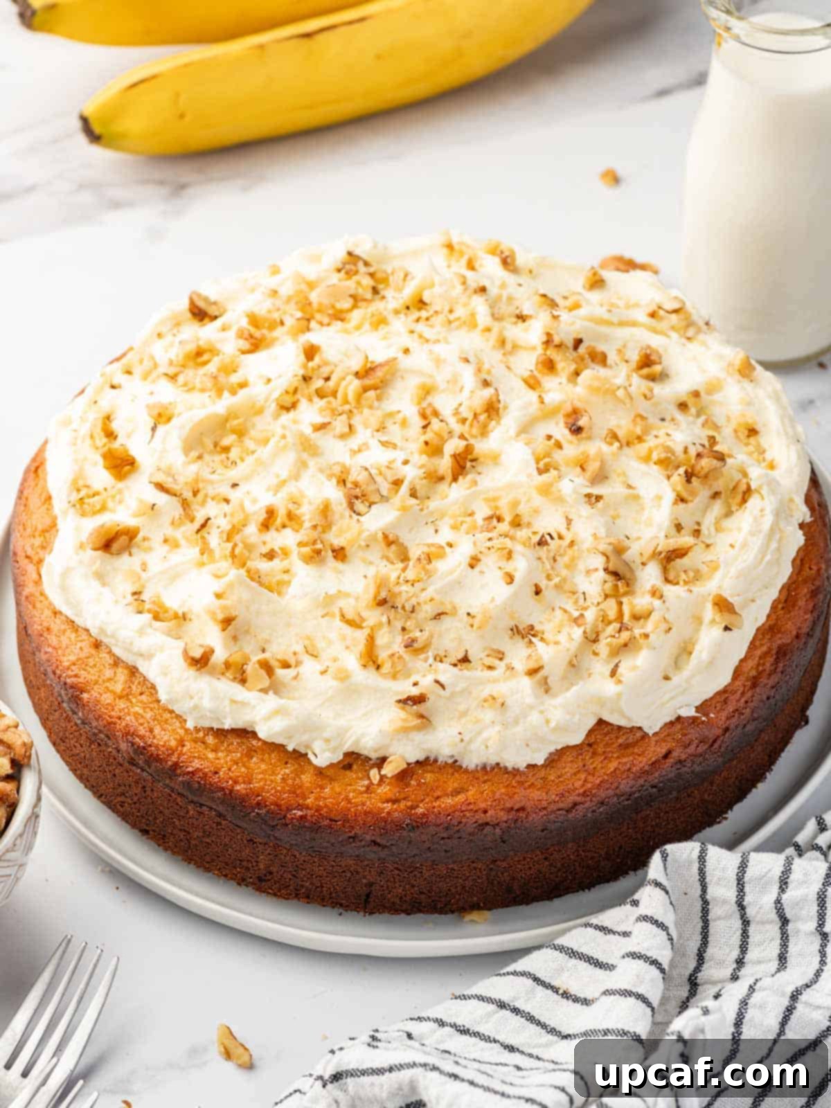 A beautifully frosted banana walnut cake, topped with chopped walnuts, sitting on an elegant platter.