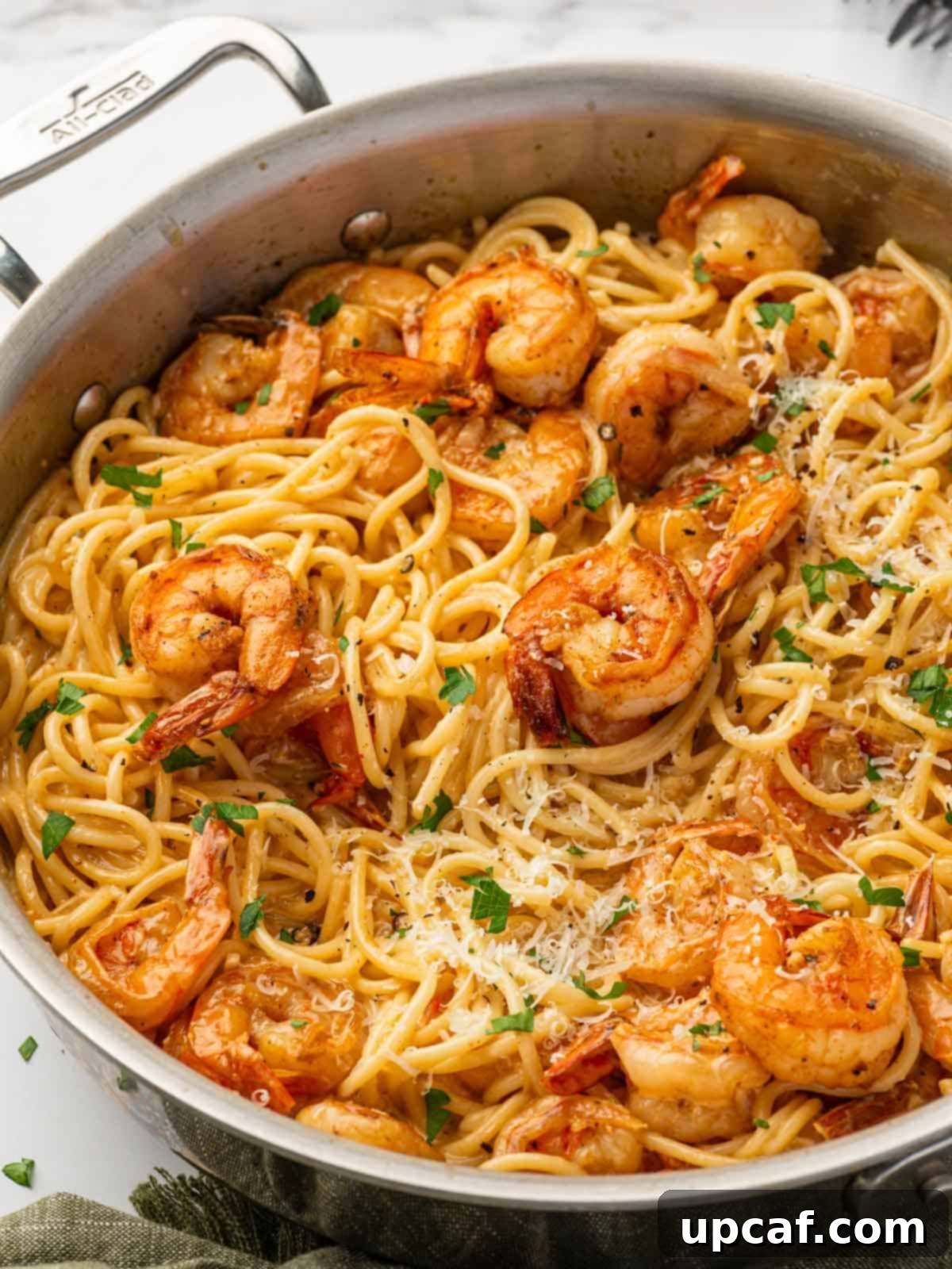 A close-up of Cajun shrimp scampi with tender shrimp and pasta in a skillet, garnished with fresh herbs.