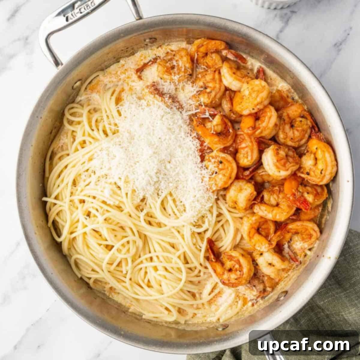 Cooked spaghetti, shrimp, and Parmesan cheese being tossed with the creamy Cajun sauce in a skillet.