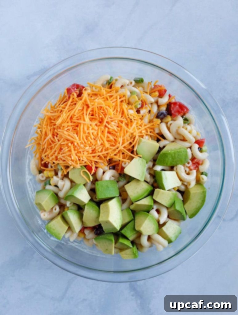 All the ingredients for Taco Ranch Pasta Salad, including cooked pasta, diced vegetables, beans, and shredded cheese, combined in a large glass mixing bowl before dressing.