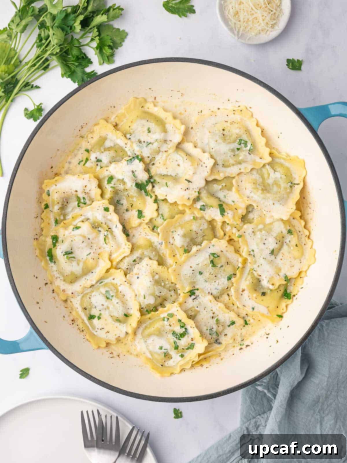 Spinach and ricotta ravioli with cream sauce in a dutch oven, garnished with fresh herbs.