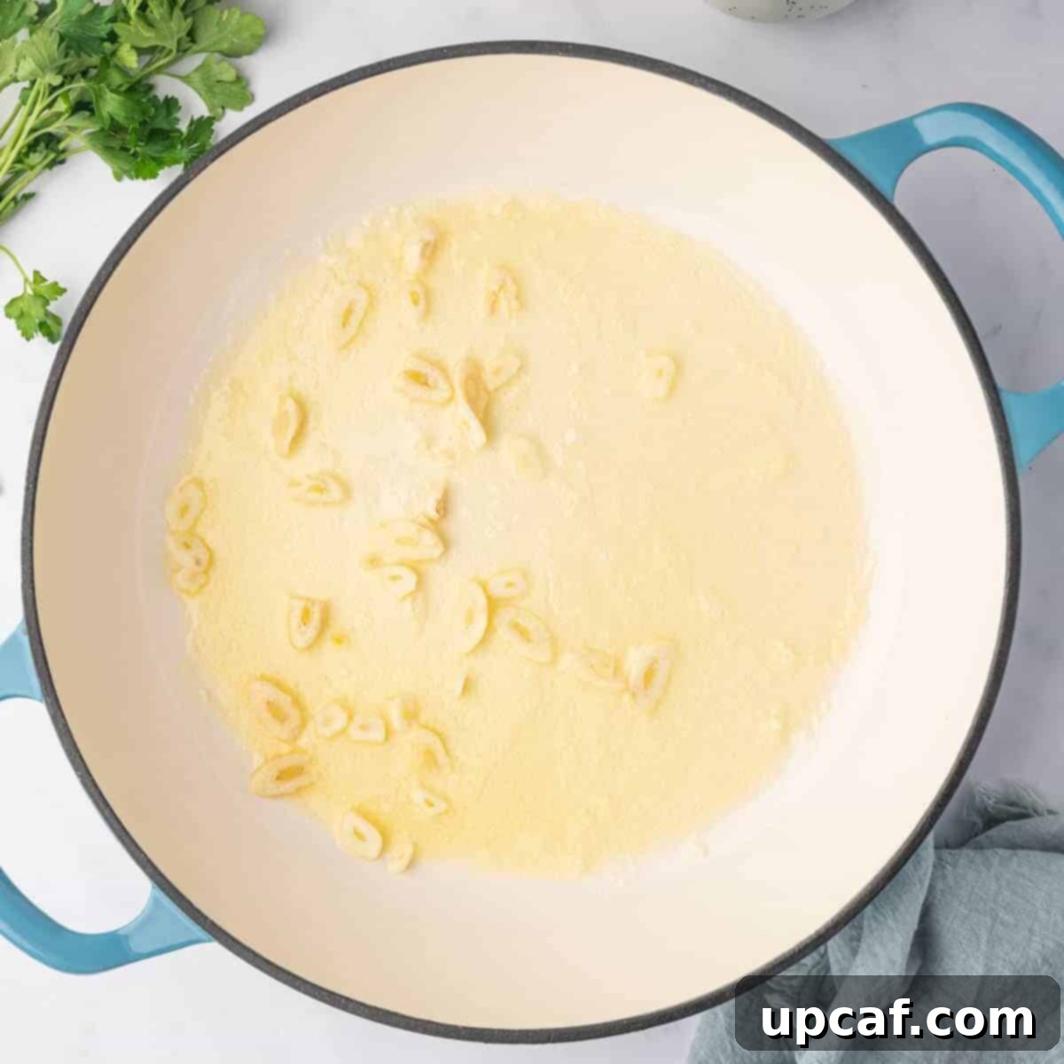 Adding sliced garlic to the cream sauce in a skillet.