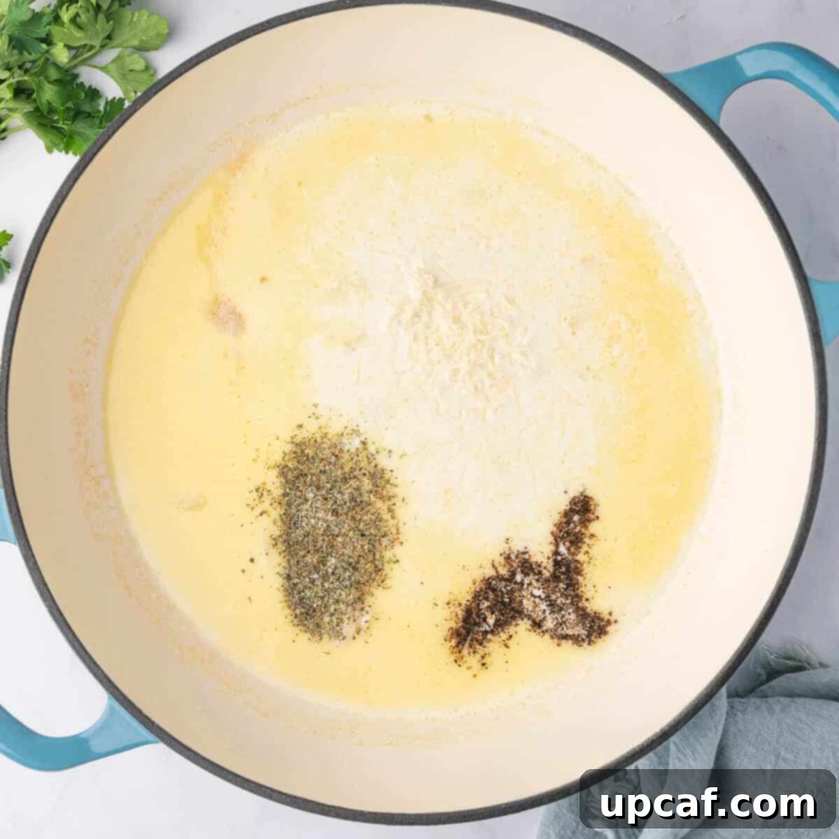 Seasoning the cream sauce for ravioli with Italian herbs, salt, and pepper.