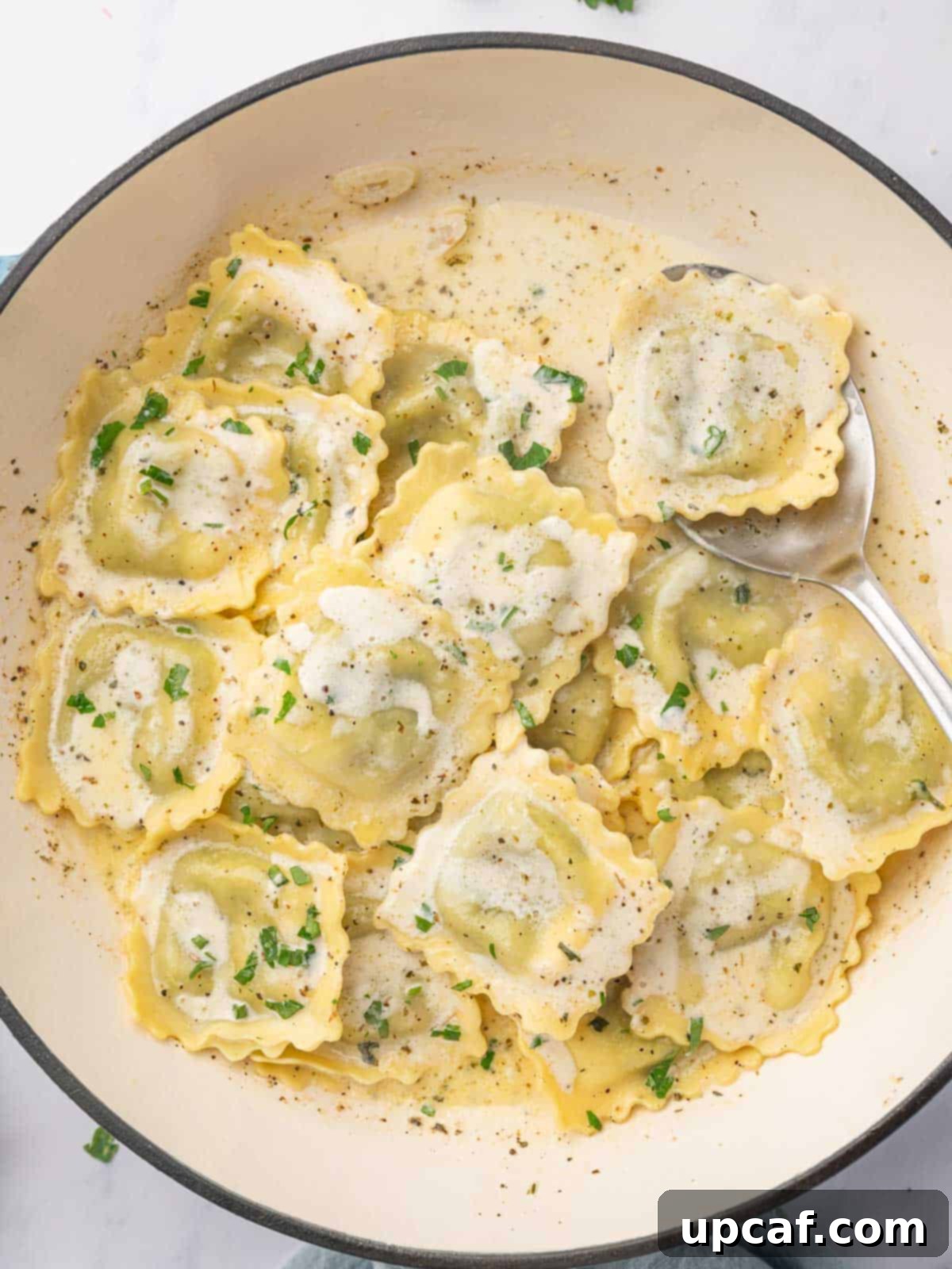 A spoon serves a piece of spinach and ricotta ravioli from a dutch oven, highlighting the creamy sauce.