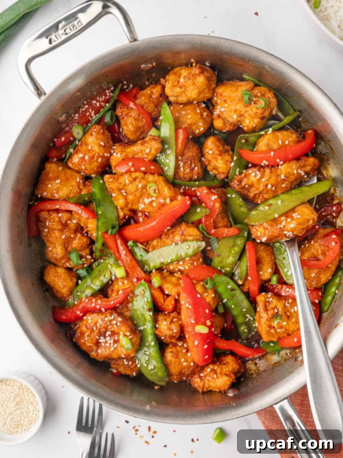 Crispy Honey Chilli Chicken served with vegetables, garnished with sesame seeds and green onions.