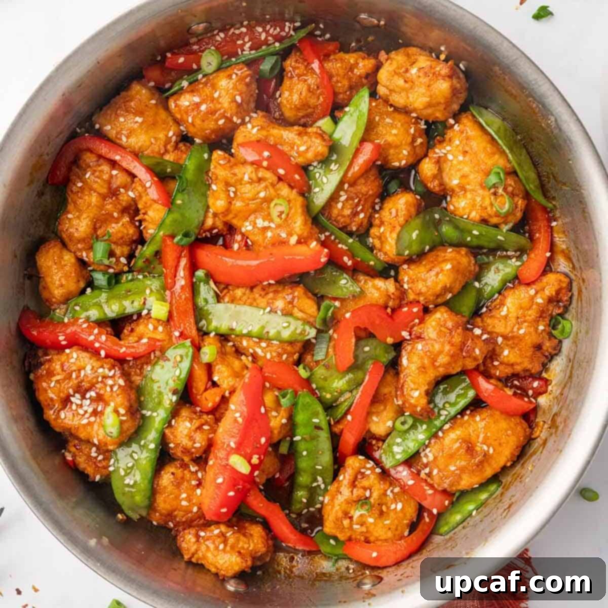A skillet filled with finished crispy honey chili chicken and vegetables, garnished with sesame seeds.