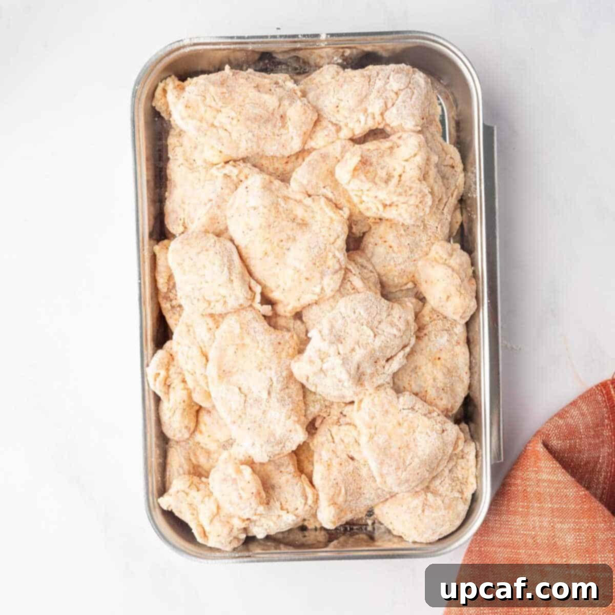 Flour-coated raw chicken breast pieces arranged neatly on a tray before frying.
