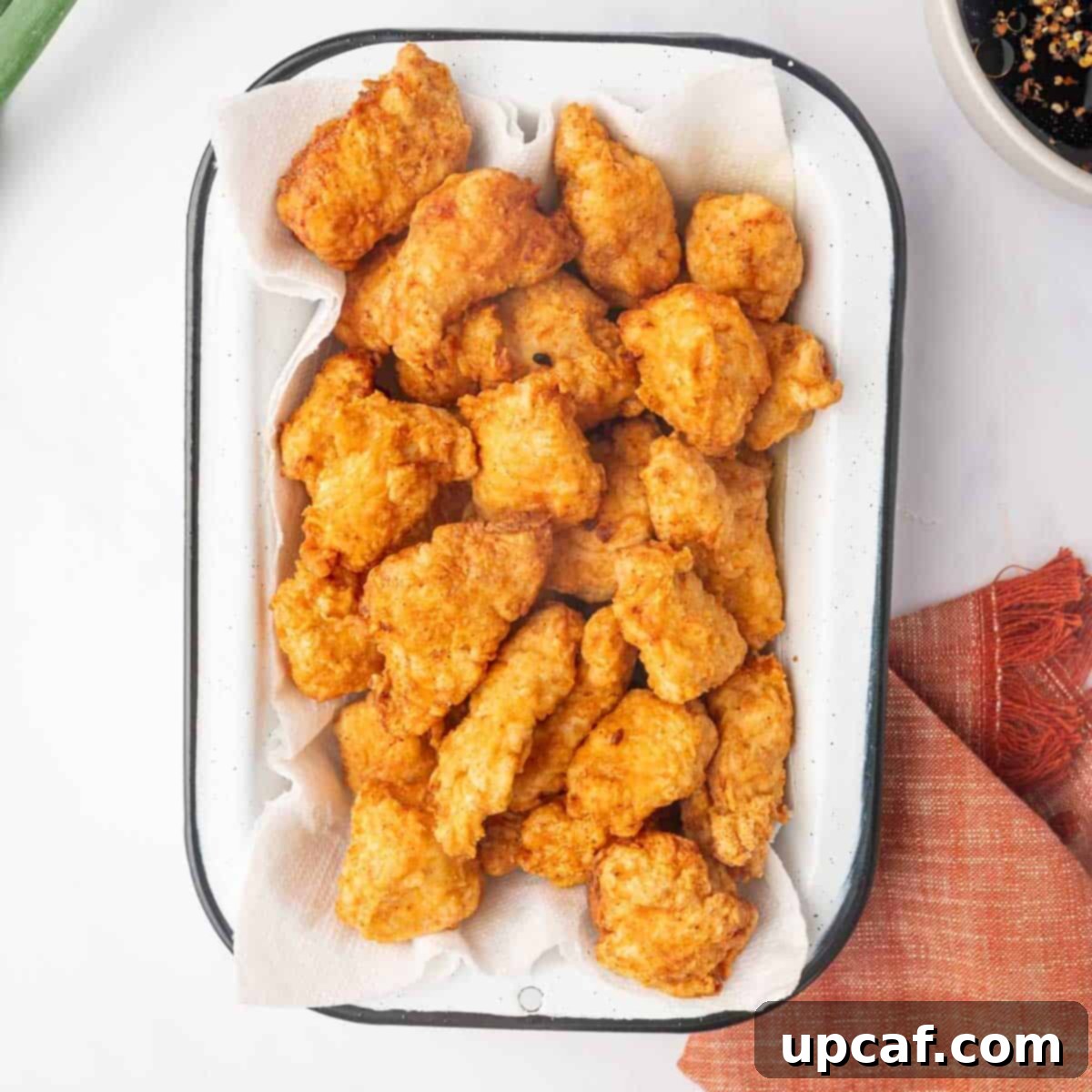 Freshly fried golden brown chicken pieces draining on a paper towel-lined tray.