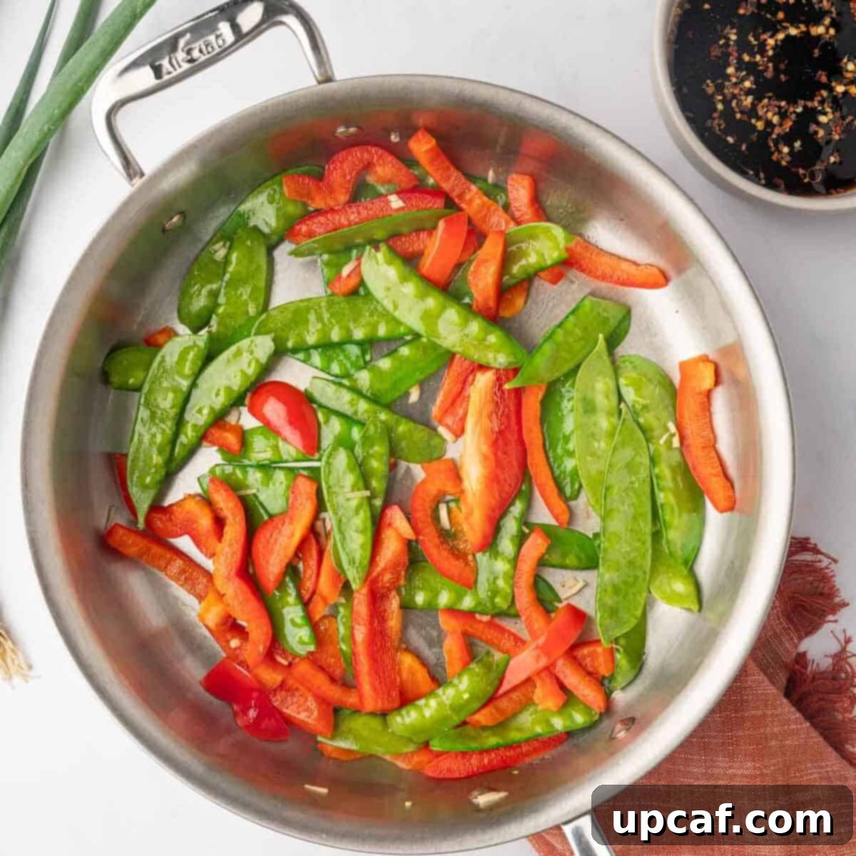 Sauteed sliced red bell peppers and snow peas in a skillet with garlic.