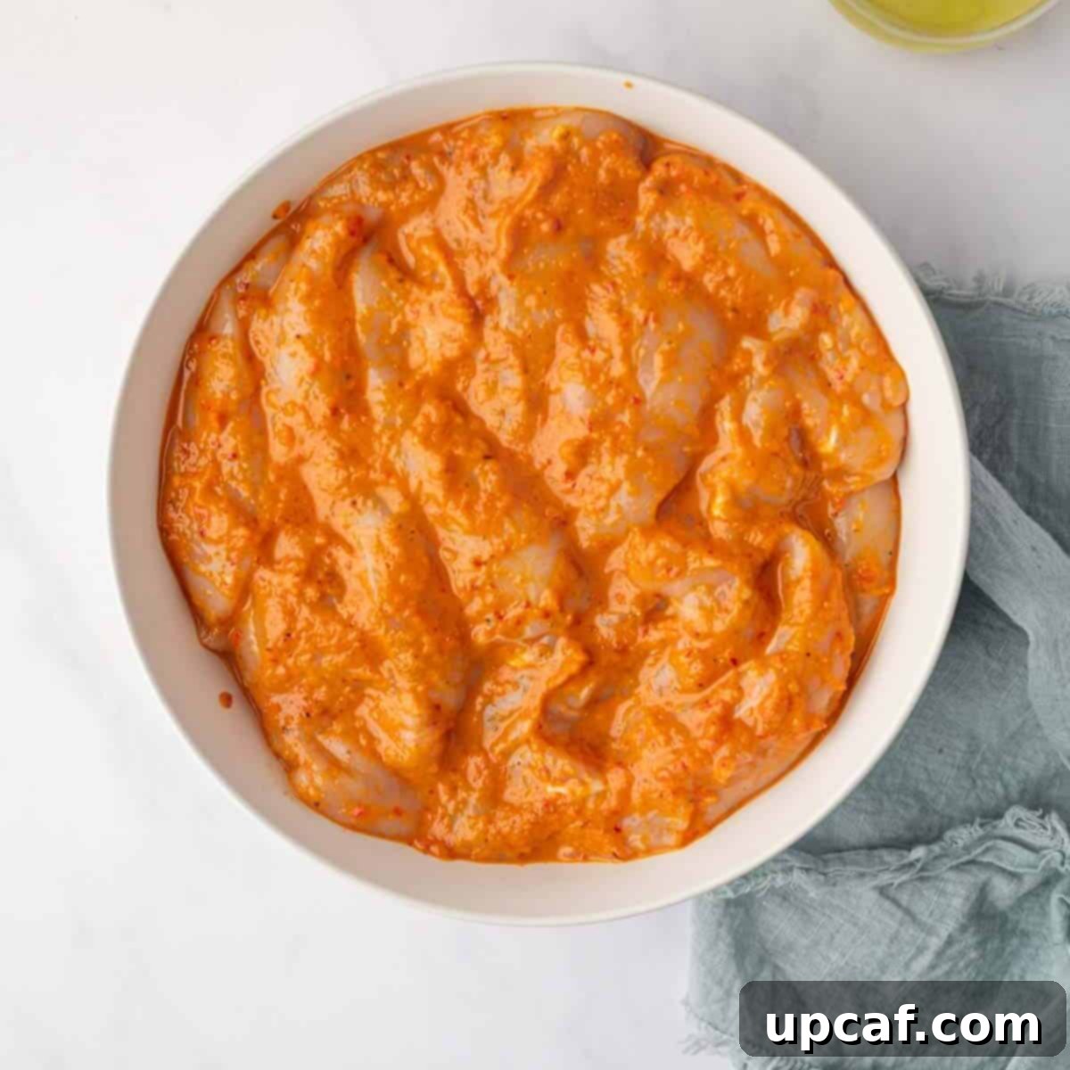 Fiery Peri Peri Chicken 7 Chicken pieces marinating in a rich, red peri peri sauce in a bowl.