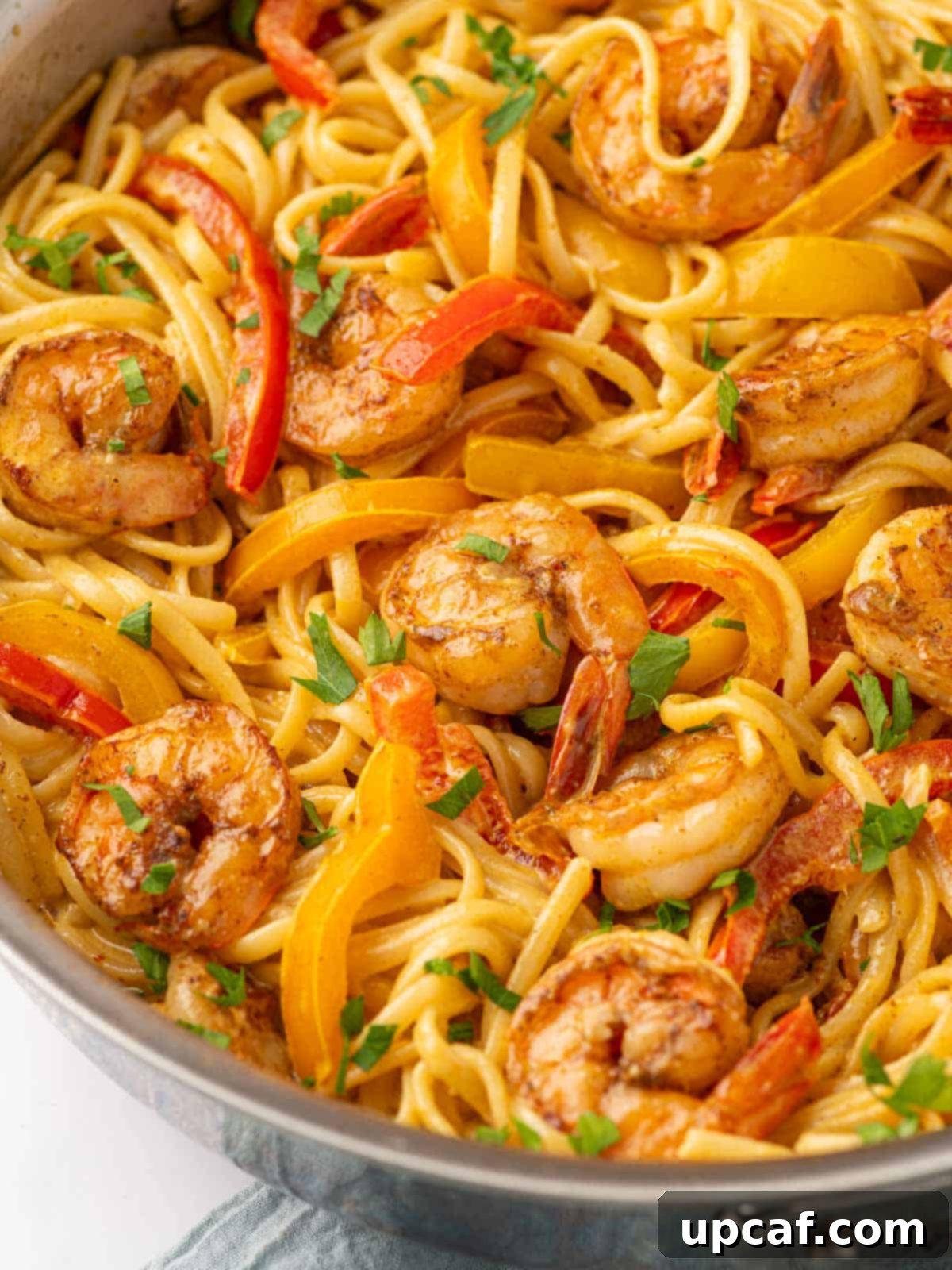 One Love Shrimp Pasta 11 Close-up of a vibrant serving of Jamaican Shrimp Rasta Pasta, showcasing succulent shrimp, colorful bell peppers, and pasta coated in creamy sauce, garnished with fresh parsley.