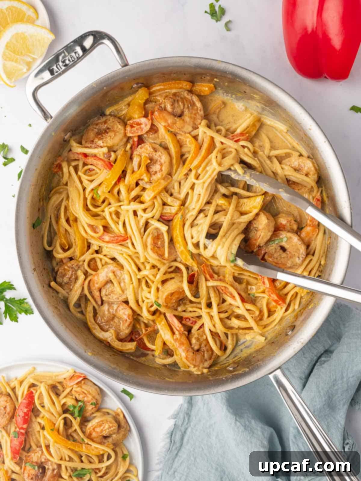 One Love Shrimp Pasta 10 Tongs gently scooping a generous serving of Jamaican Shrimp Rasta Pasta, laden with shrimp, colorful peppers, and creamy sauce, from a large skillet.