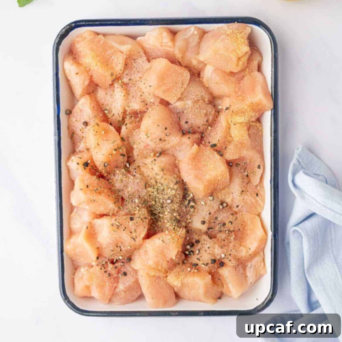 Seasoned chicken pieces ready for cooking on a tray.