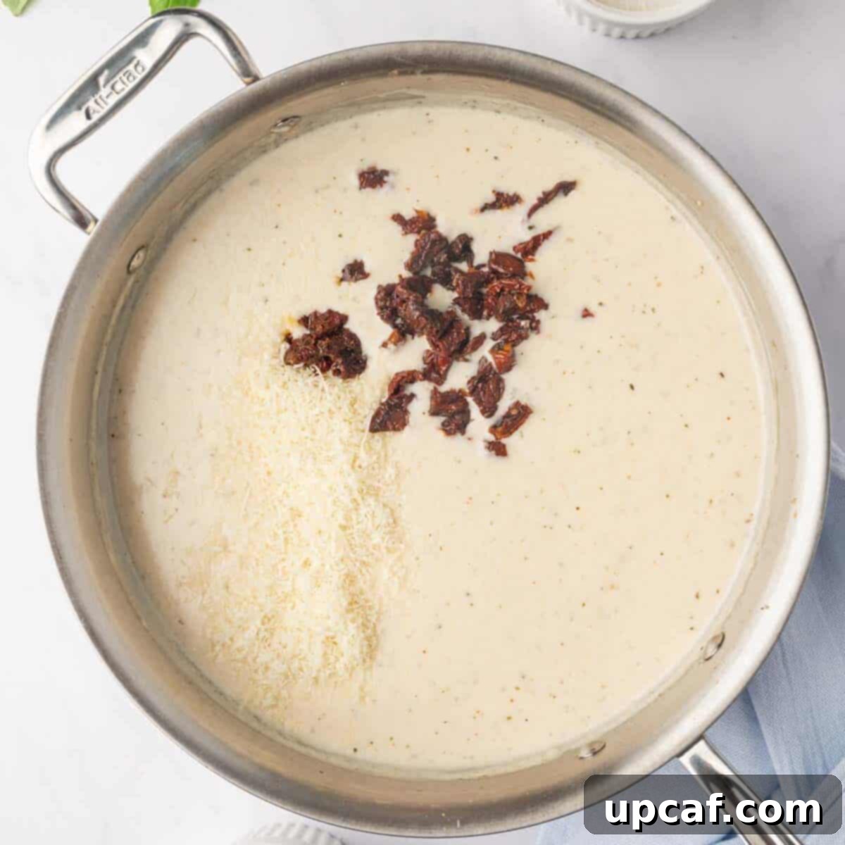 Adding sun-dried tomatoes and Parmesan cheese to the simmering cream sauce.