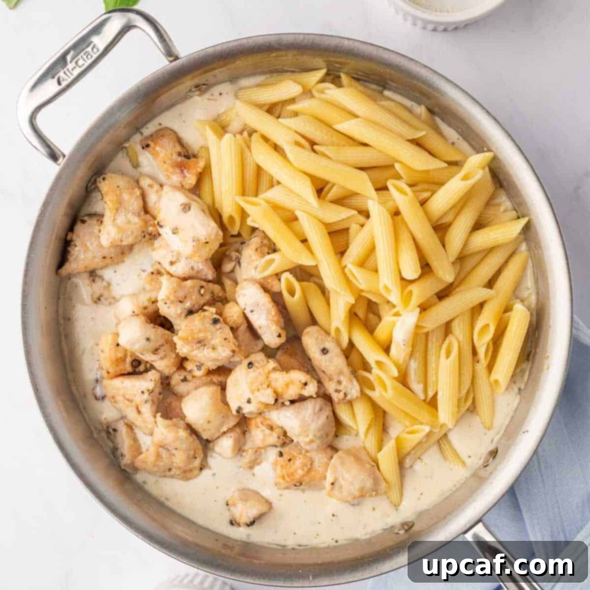 Combining cooked chicken, pasta, and the creamy sun-dried tomato sauce in a large skillet.