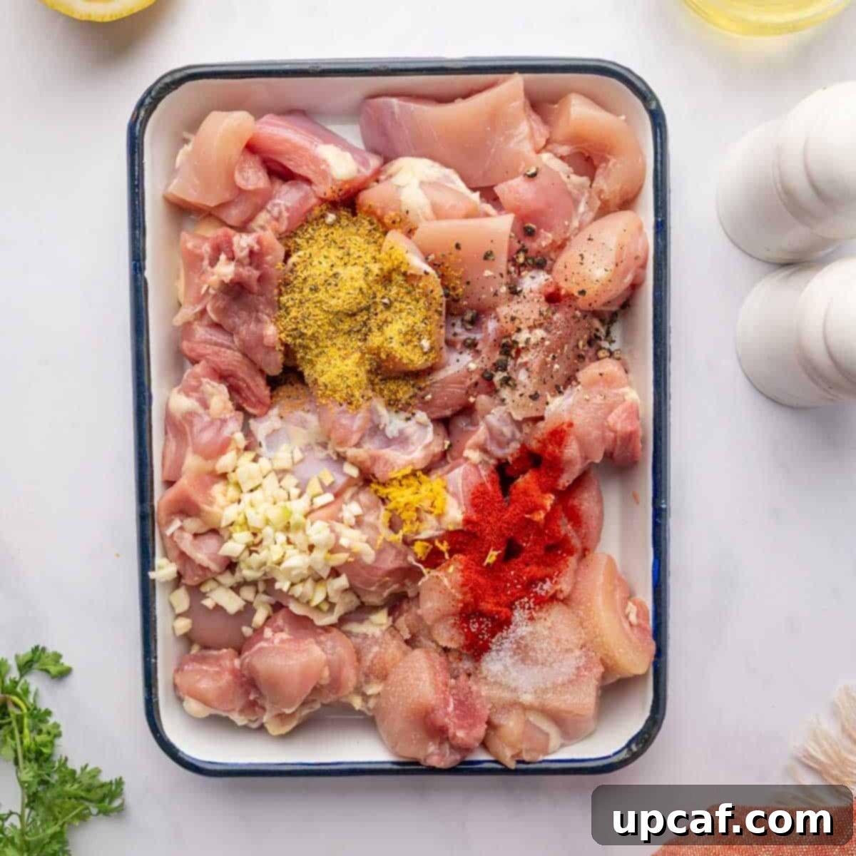 Chicken pieces being mixed with garlic, lemon pepper seasoning, and other spices in a bowl, preparing for marinade.