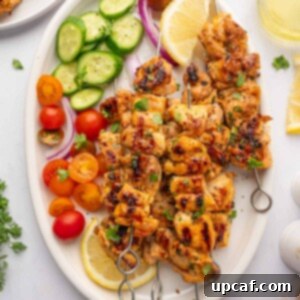 Fresh veggies and lemon wedges surround grilled chicken skewers on a platter, highlighting the vibrant presentation.