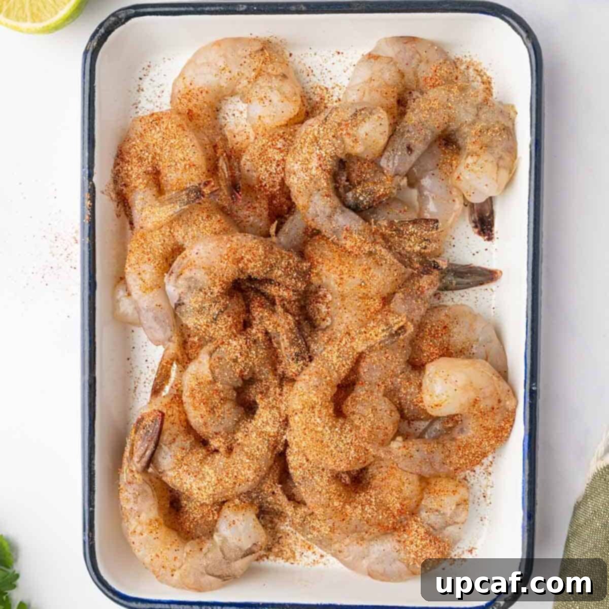 Seasoned shrimp on a platter, evenly coated with spices and olive oil, ready for grilling.