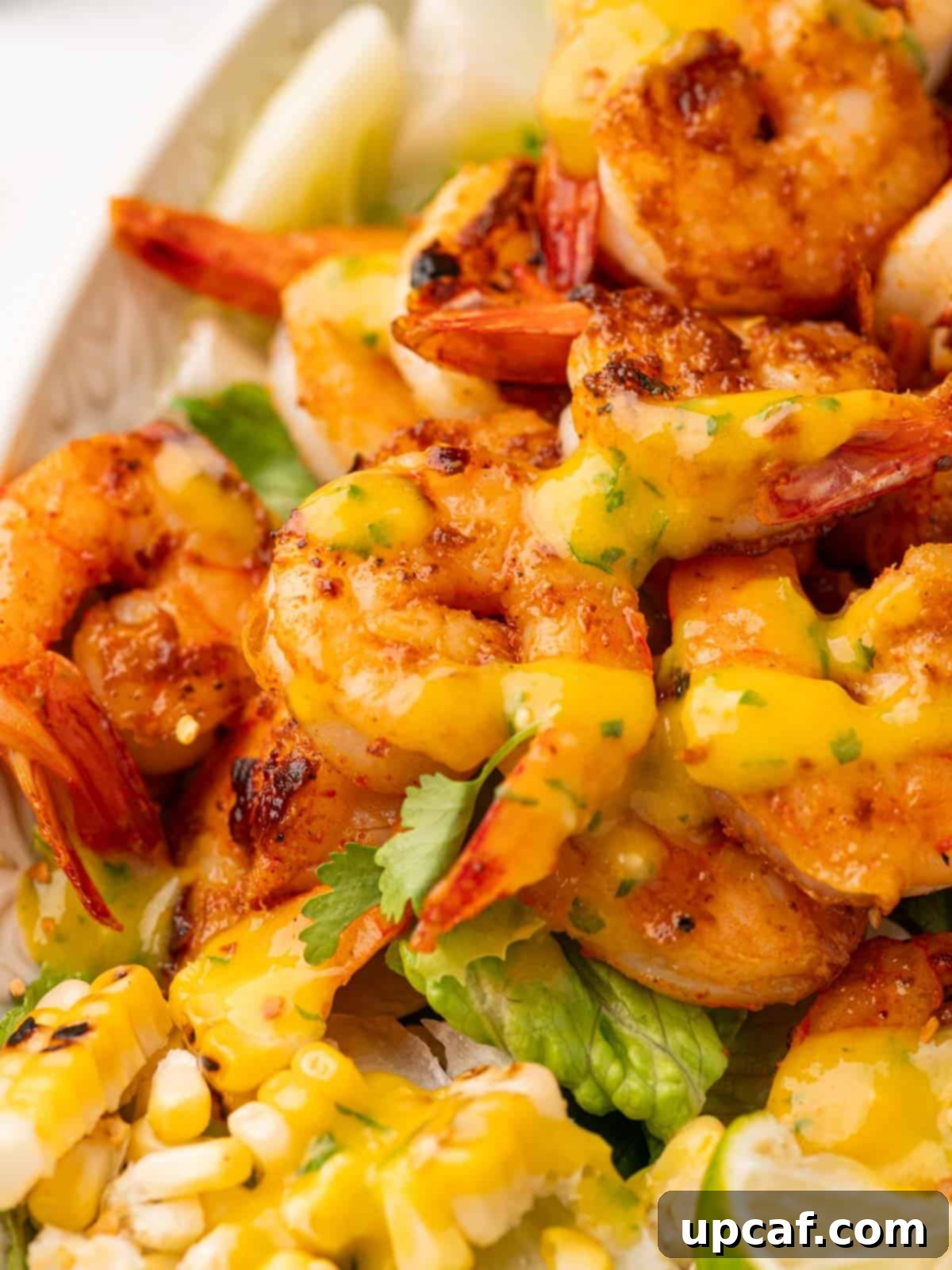 Close up of perfectly cooked shrimp drizzled with the vibrant mango salad dressing, highlighting the texture and color.