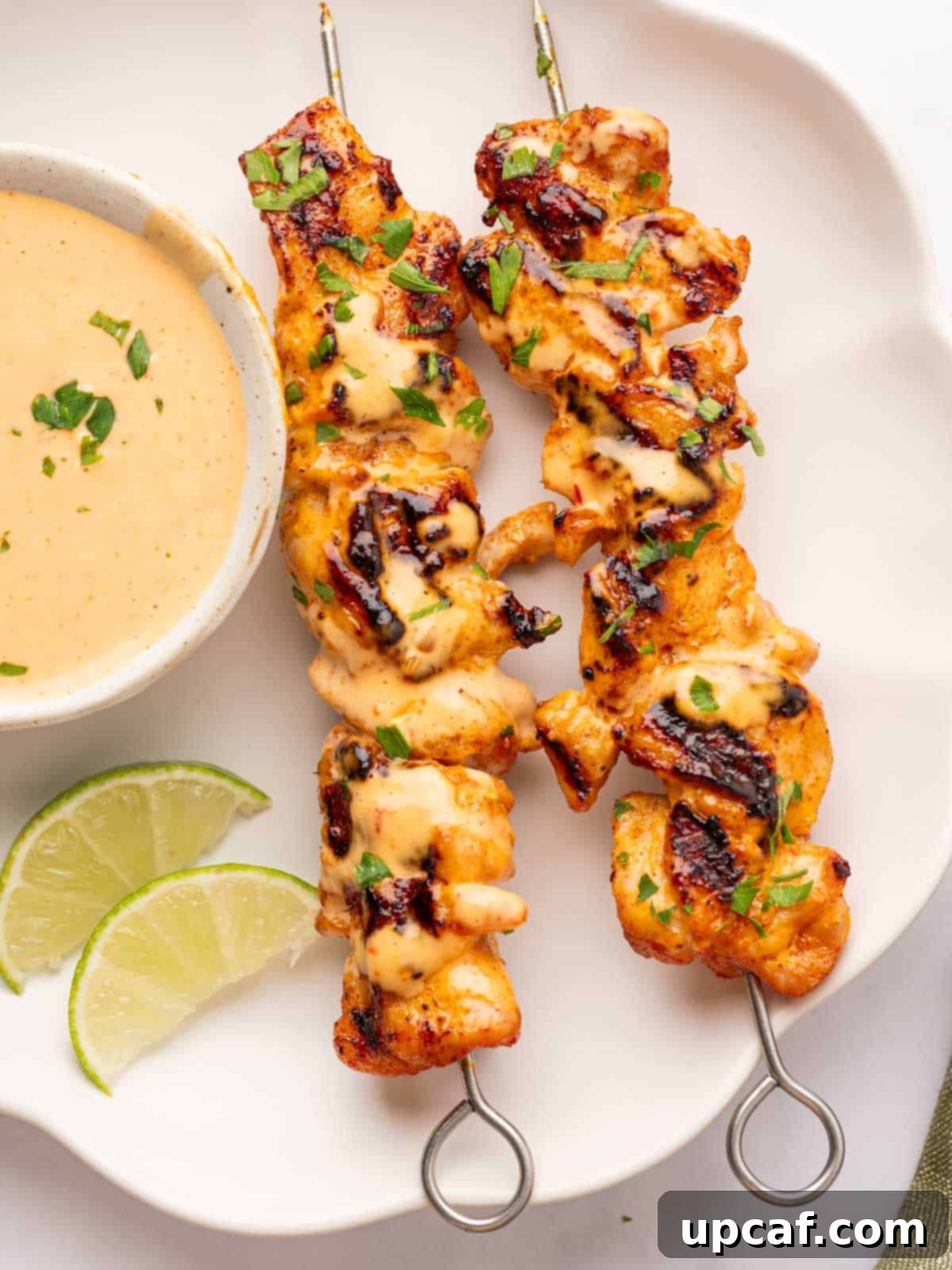 Dynamite Chicken Skewers 9 A close-up of a serving of Bang Bang Chicken Skewers on a white plate, garnished with fresh herbs.