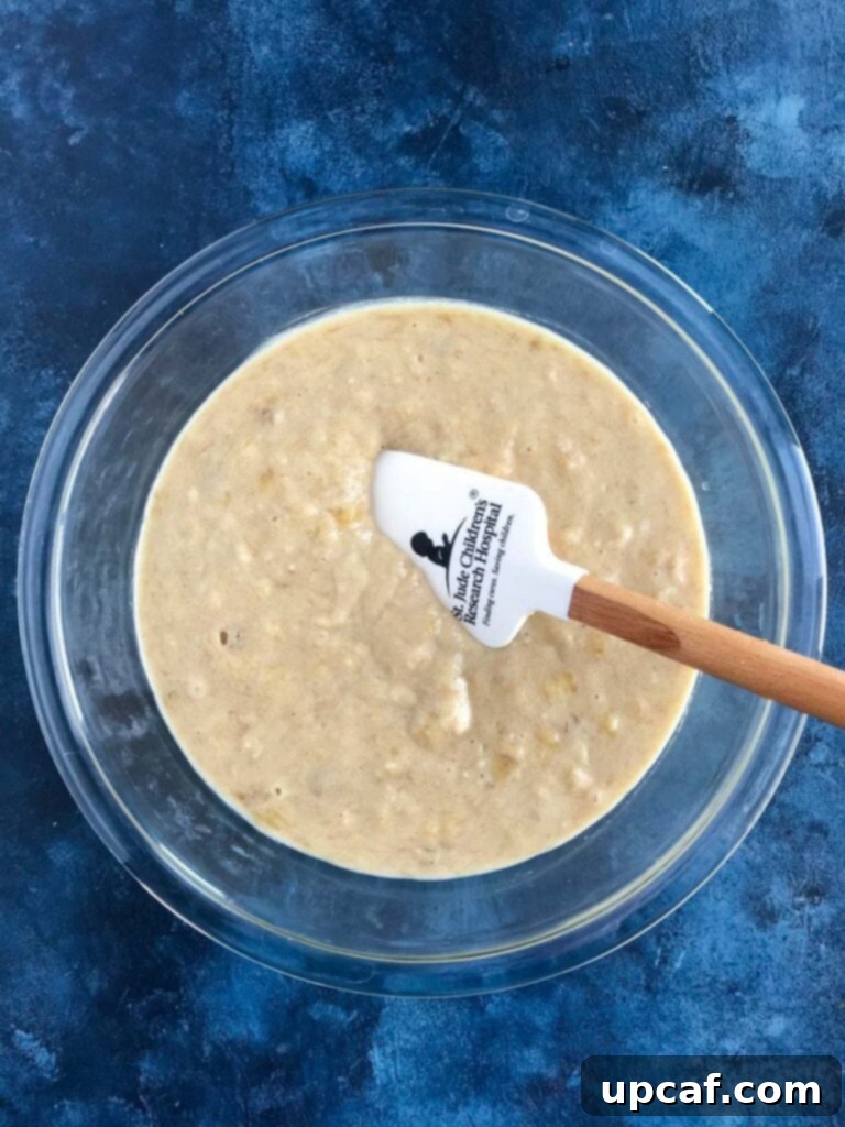 Marbled Nutella Banana Muffins 2 Wet ingredients for banana muffins (mashed bananas, egg, sugar, vanilla, yogurt, melted butter) in a bowl, with a whisk.