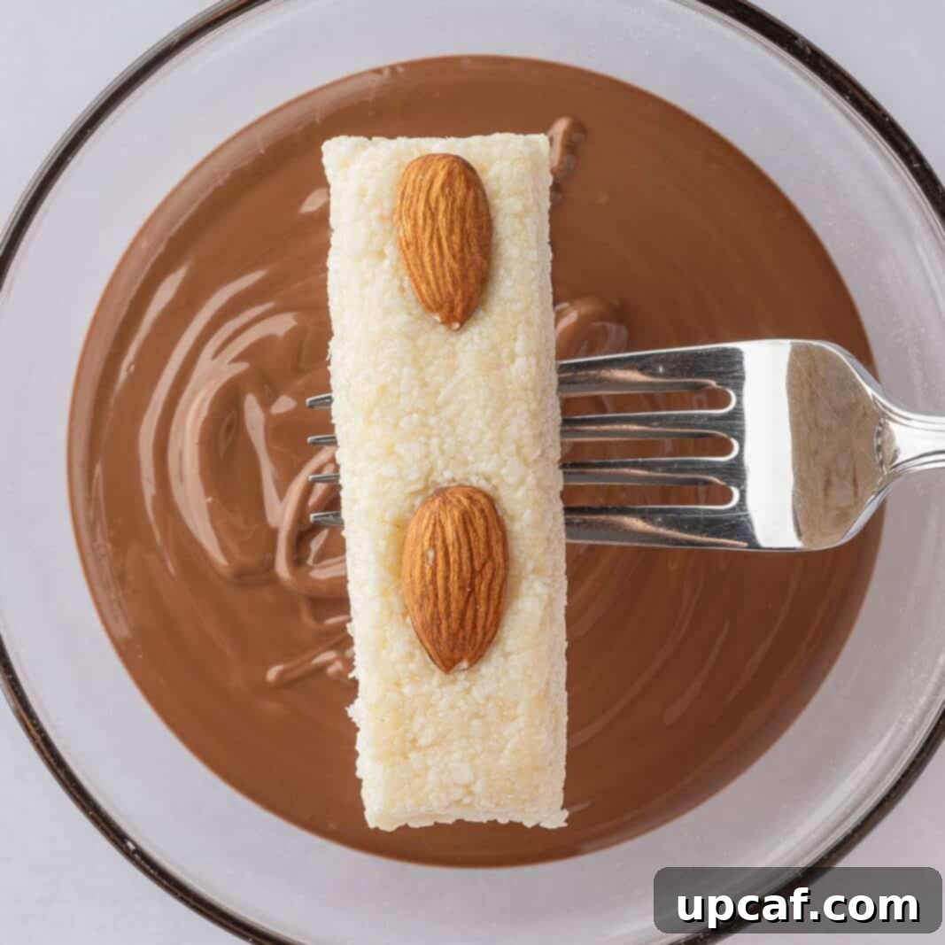 Island Coconut Chocolate Dream 7 A fork is used to dip a cut candy bar filling into a bowl of perfectly melted chocolate, ensuring a smooth coating.