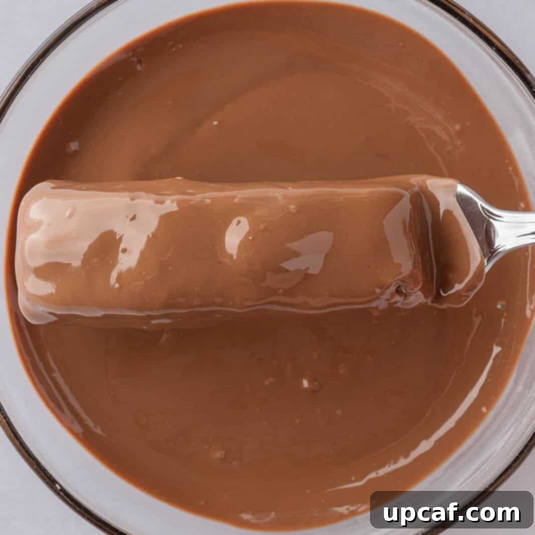 Island Coconut Chocolate Dream 8 A candy bar is fully coated in melted chocolate, with excess chocolate dripping off, before being placed on parchment paper.