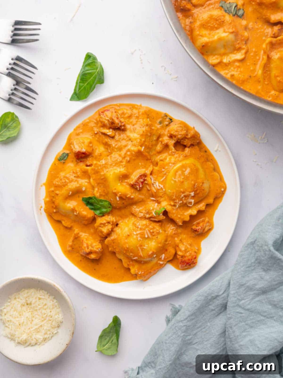 Decadent Lobster Ravioli Sauce 2 A serving of lobster ravioli drenched with sauce for lobster ravioli, with a bowl of fresh parmesan beside it.