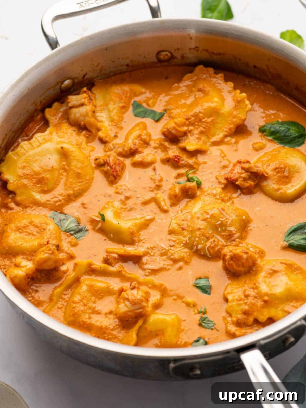 Decadent Lobster Ravioli Sauce 10 A sauce pan with tomato cream sauce, ravioli and chucks of lobster simmer on the stove.