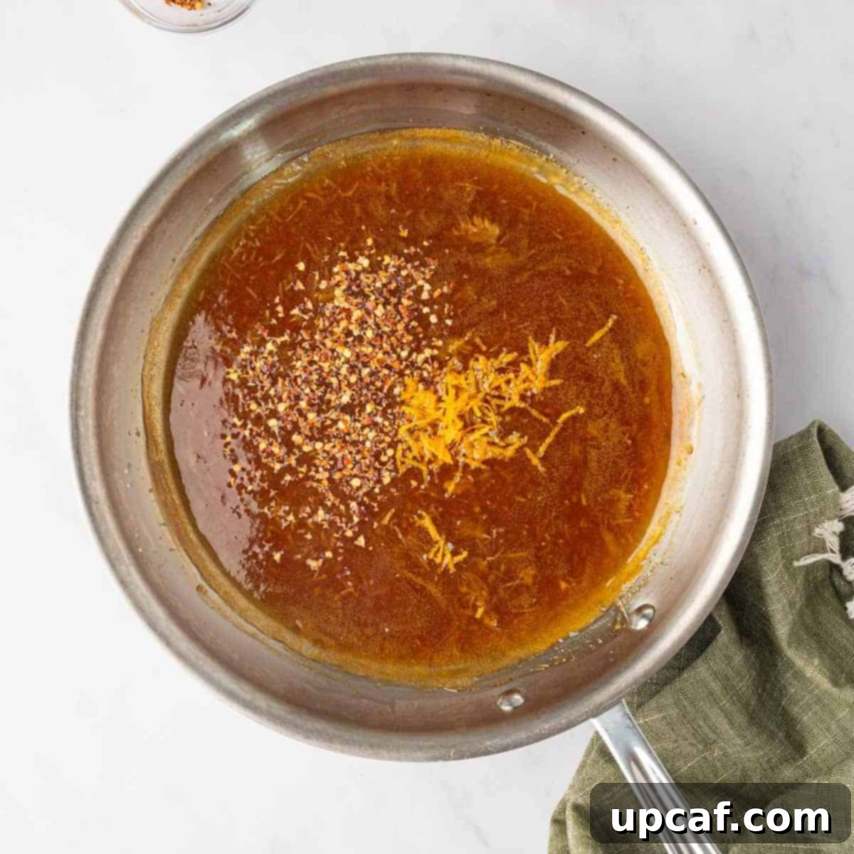 Orange zest being added to the simmering orange chicken sauce in a skillet.