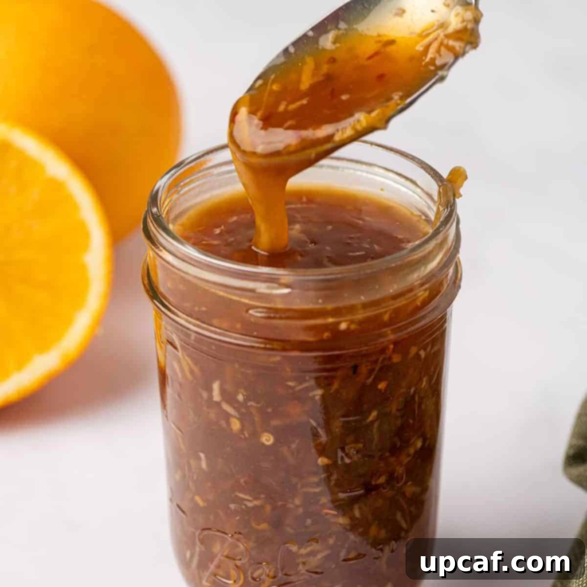 A spoon scooping perfectly thickened homemade orange chicken sauce from a small glass jar.