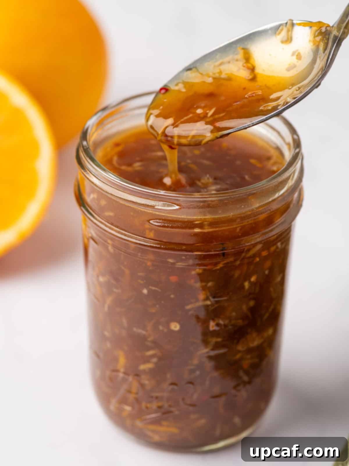 A spoon dipping into a jar of orange chicken sauce, showcasing its glossy texture.