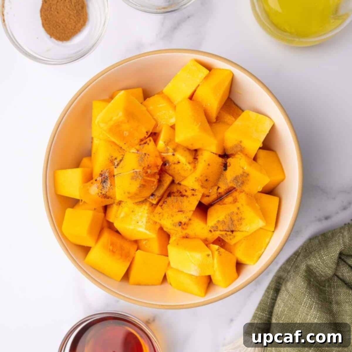 Roasted Butternut Feta Salad 4 Cubed butternut squash is seasoned with olive oil, maple syrup, salt, pepper, and cinnamon in a mixing bowl, ready for roasting.