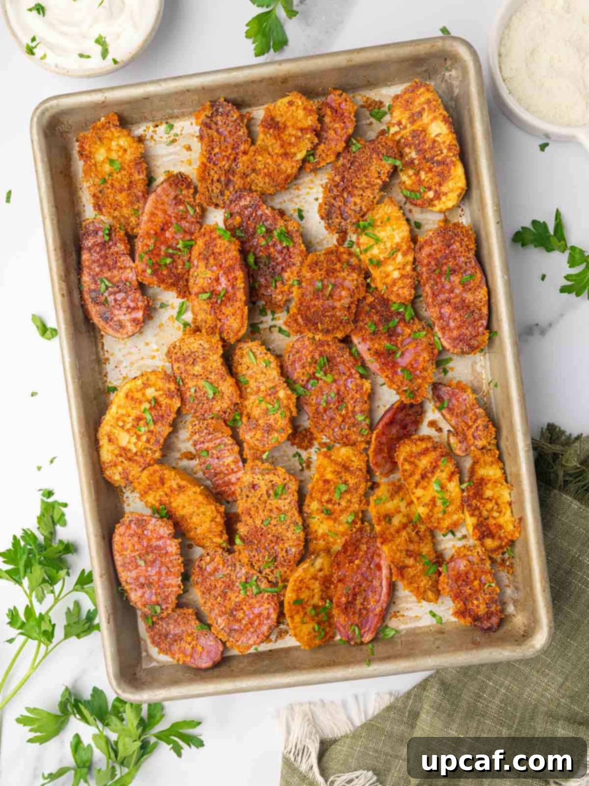 Cheesy potatoes garnishes with parsley line a baking tray.