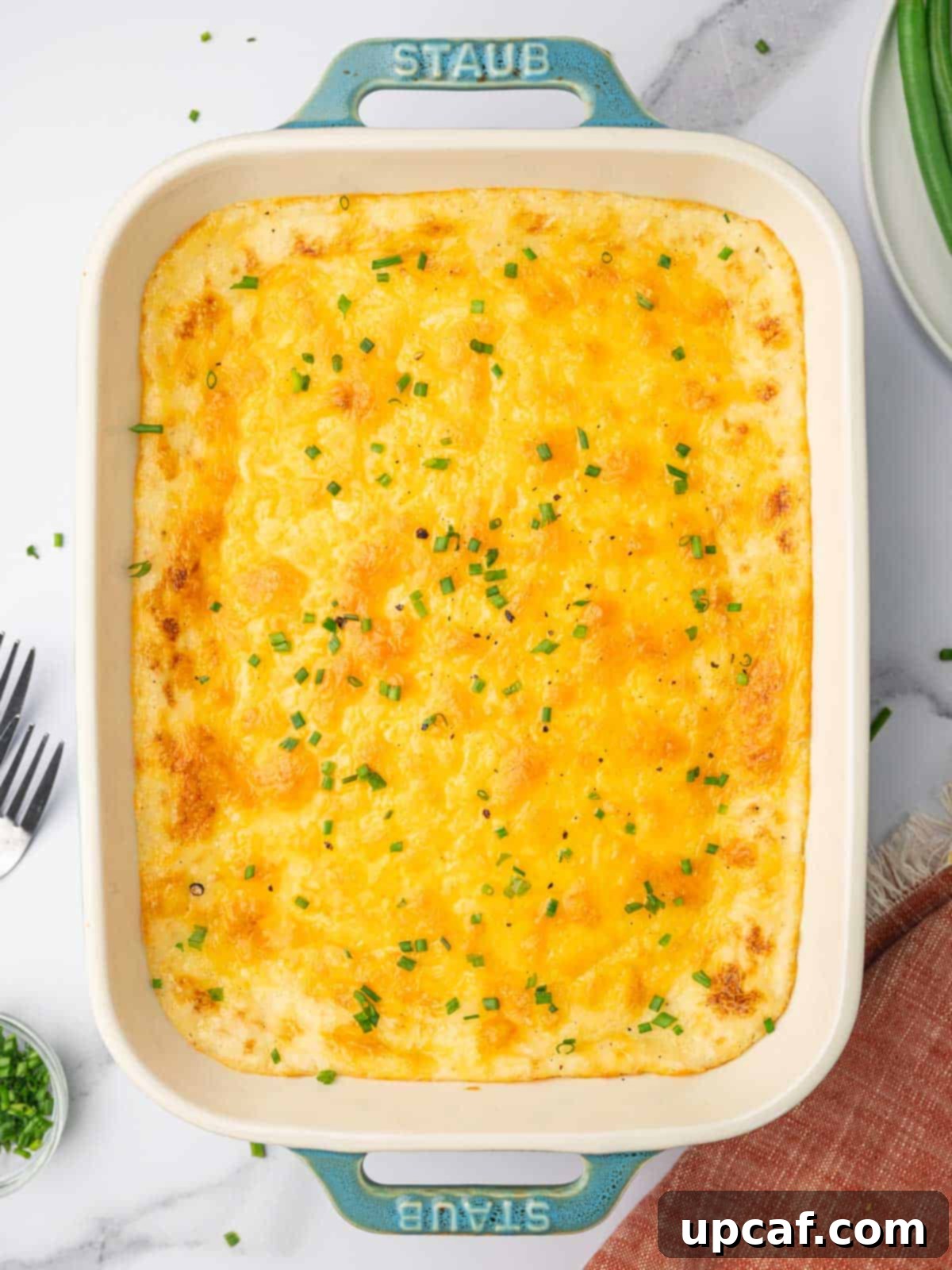 Decadent Cheesy Mash 2 A casserole dish filled with a golden-baked cheesy mashed potatoes recipe, topped with melted cheddar and fresh chives.