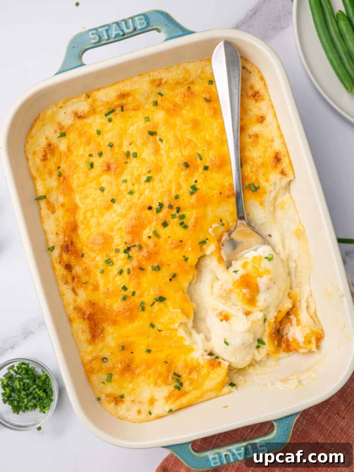 Decadent Cheesy Mash 11 A large serving spoon scoops a generous portion of cheesy mashed potatoes from a casserole dish, showing the melted cheese and creamy texture.