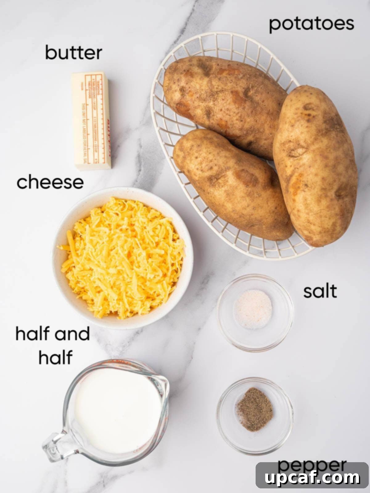 Decadent Cheesy Mash 3 A flat lay of ingredients needed for cheesy mashed potatoes recipe, including russet potatoes, butter, half-and-half, cheddar cheese, salt, pepper, and fresh chives.