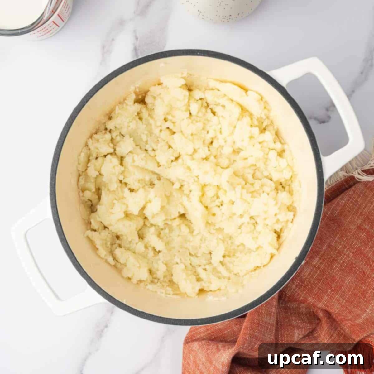 Decadent Cheesy Mash 5 Cooked potatoes have been mashed in a pot with a potato masher.