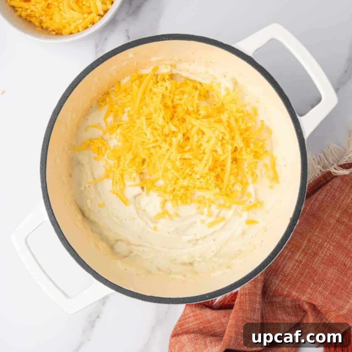 Decadent Cheesy Mash 7 Shredded cheese is added to the creamy mashed potatoes in a pot.