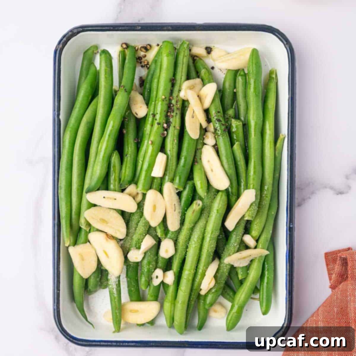 Fresh green beans are tossed in a large bowl with olive oil, sliced garlic, salt, and pepper.
