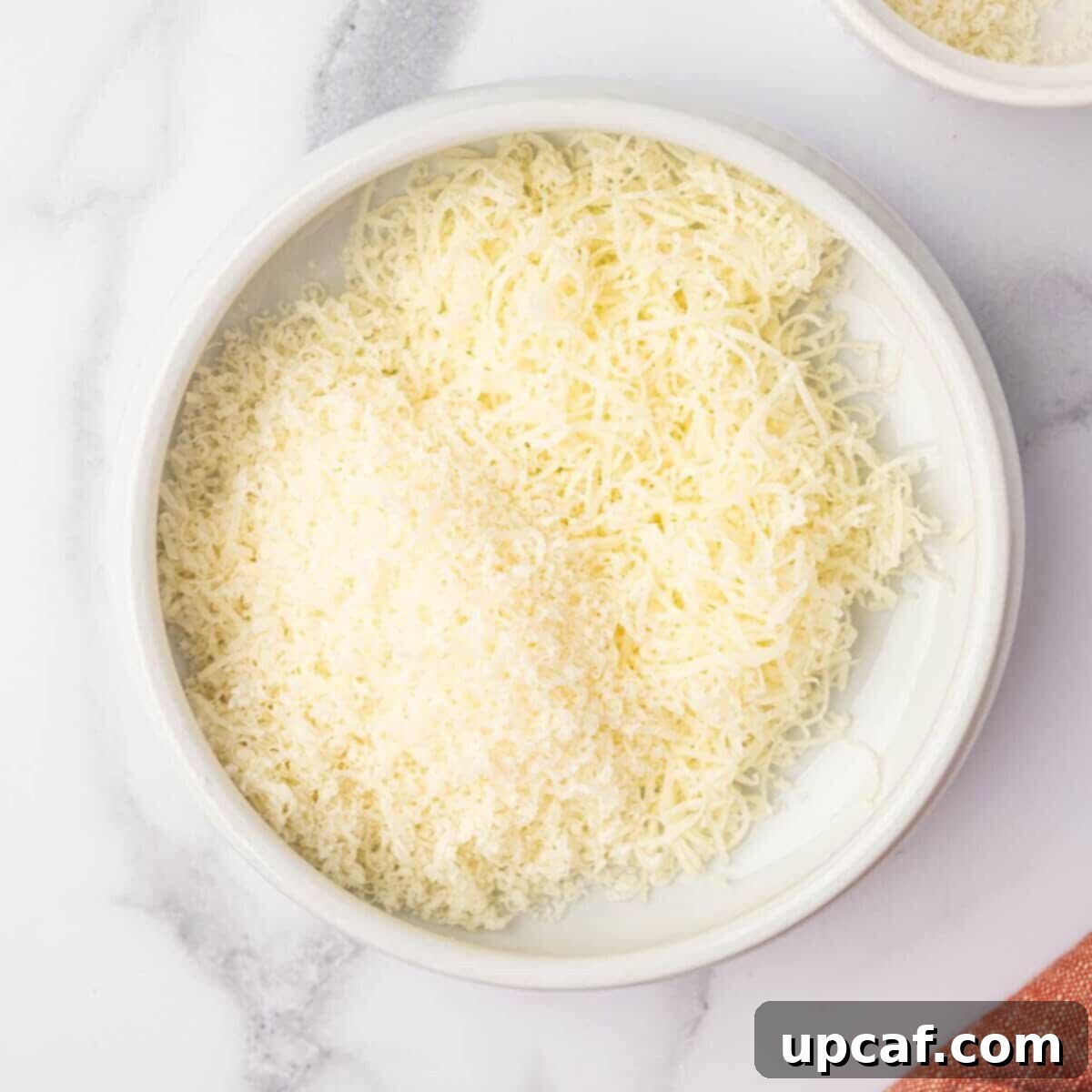 A bowl holds a mixture of freshly grated Parmesan and mozzarella cheeses.