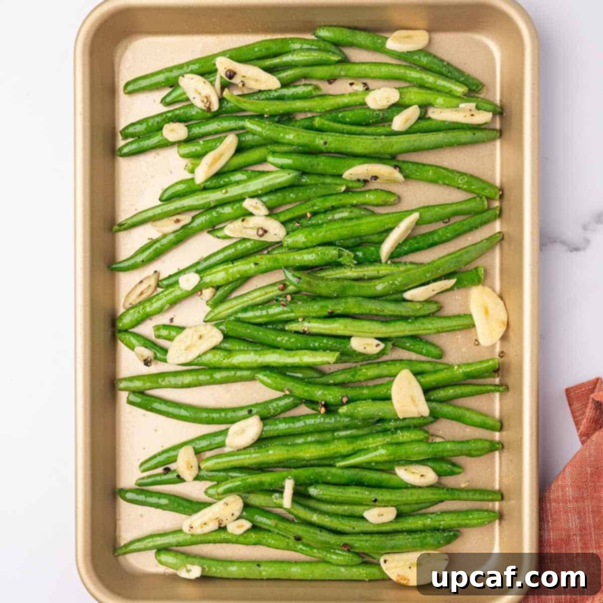 The seasoned green beans are spread in a single layer on a prepared baking sheet.