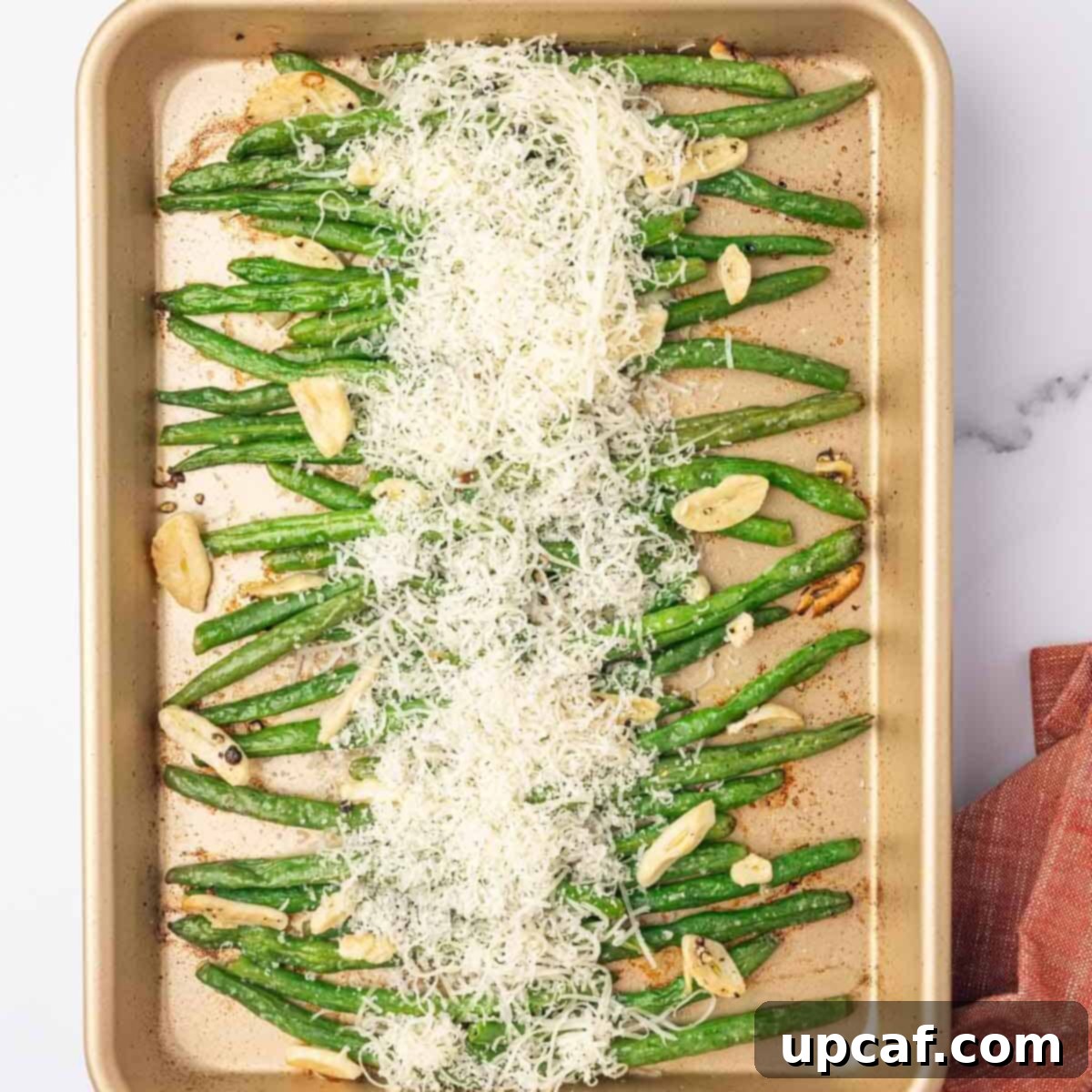 The cheese mixture is generously sprinkled over the green beans on the baking tray before baking.