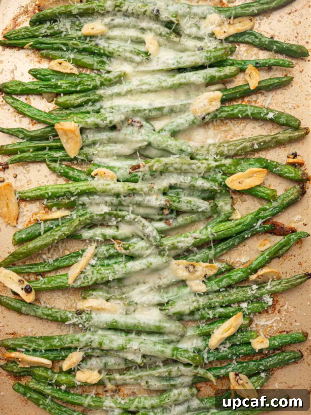 A close-up view of baked garlic parmesan green beans on a tray, showing the melted, golden cheese and tender green beans.