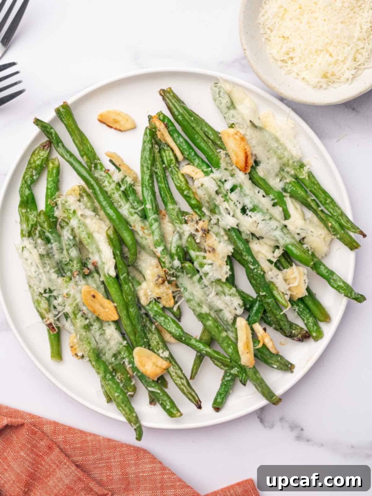 A round white serving plate filled with baked garlic parmesan green beans, garnished and ready to be enjoyed.