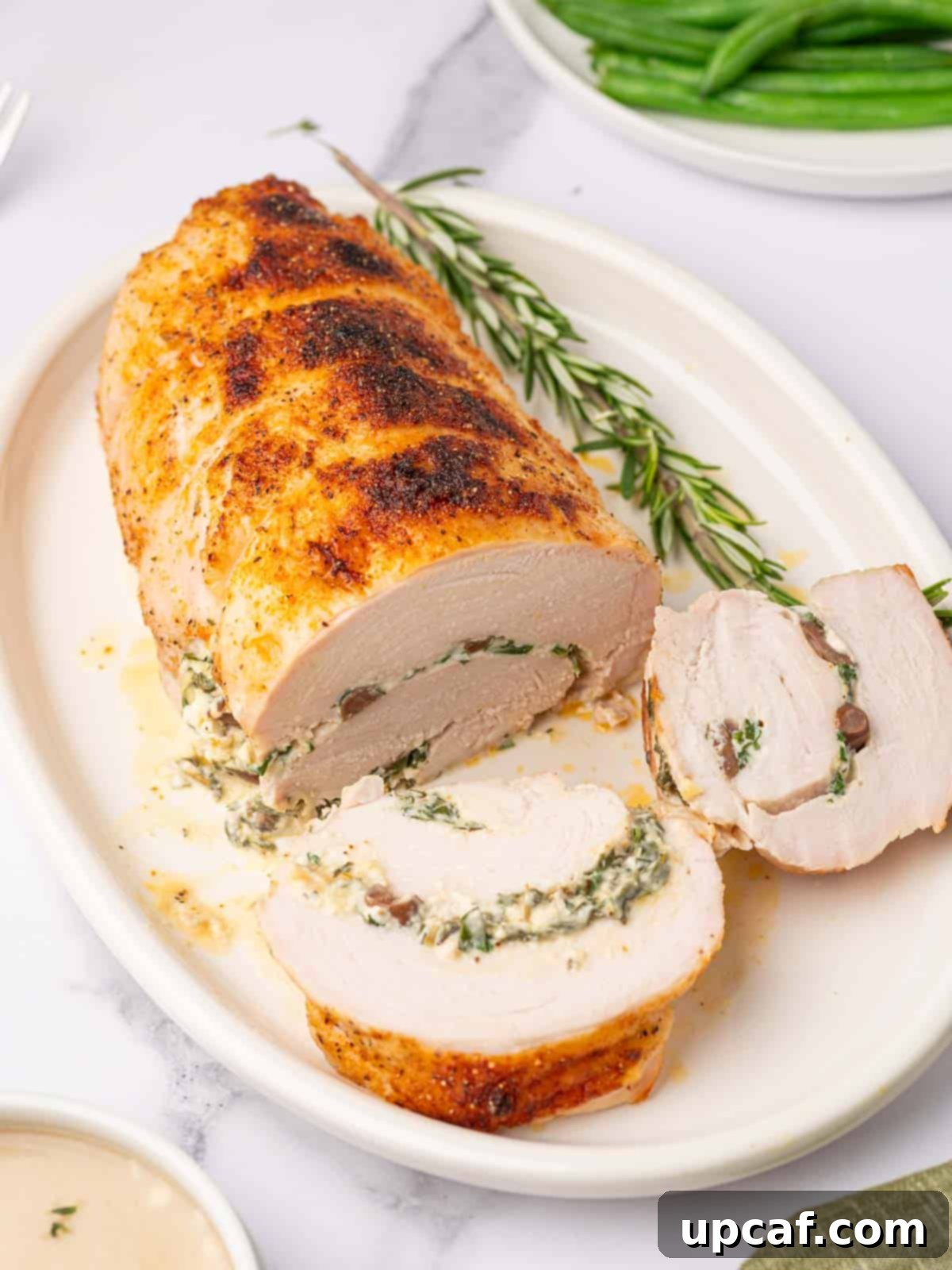 Savory Stuffed Turkey Roll 2 Two generous slices are cut from a golden brown stuffed turkey roll on an elegant serving platter, revealing the creamy spinach and olive filling.