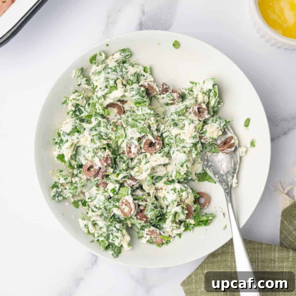 Savory Stuffed Turkey Roll 5 A spoon rests on the side of a white bowl filled with the creamy, herbaceous cheese and olive stuffing mixture, ready to be spread.