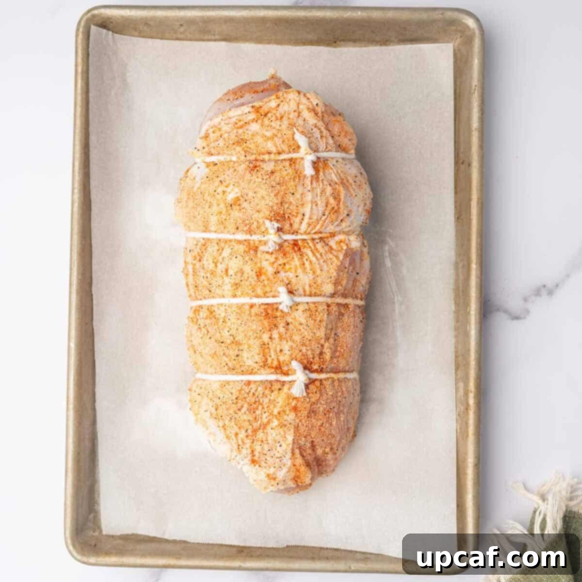 Savory Stuffed Turkey Roll 8 A neatly trussed stuffed turkey breast, secured with kitchen twine, is placed on a baking sheet, ready for the oven.